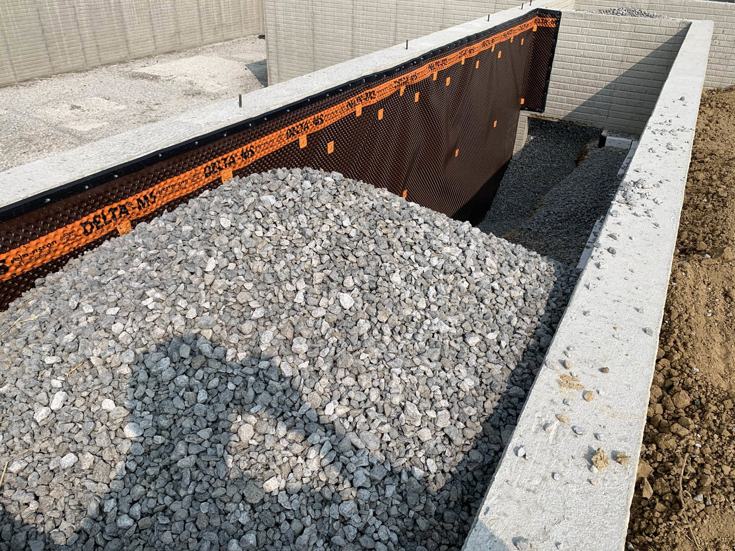 Gravel pile beside a concrete curb and brick wall on an outdoor construction site
