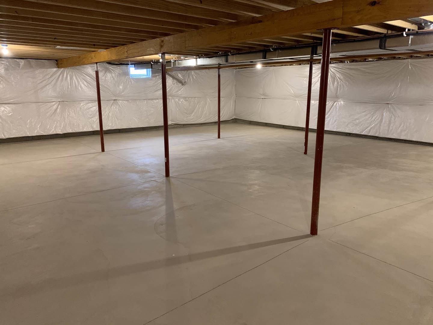 White-walled room with exposed wooden ceiling beams, concrete floor, red support pole, and window illuminated by blue light