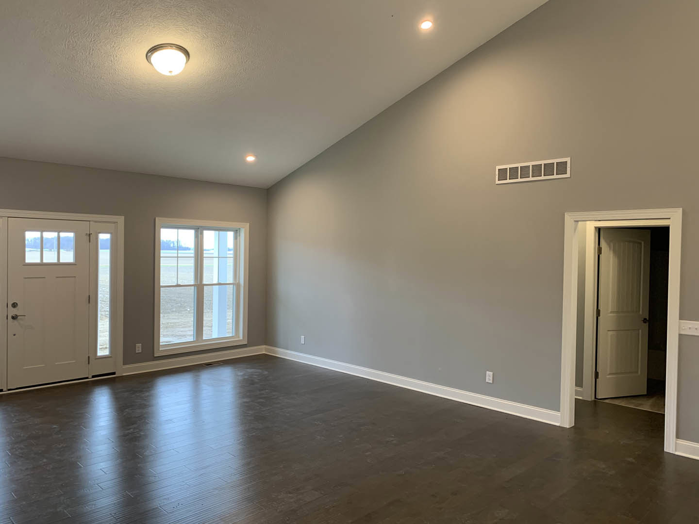 Dark wood flooring with white trim, white door featuring black knobs and glass panels, large windows offering ocean view, light fixture mounted on white ceiling.