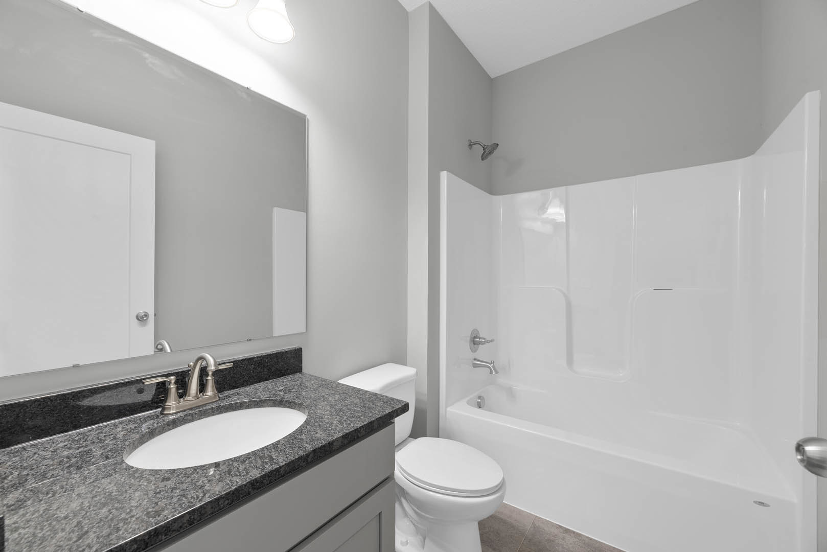 Modern bathroom with white freestanding bathtub, wall-mounted silver faucet, rectangular sink on stone countertop, light gray tile walls, and minimalistic fixtures