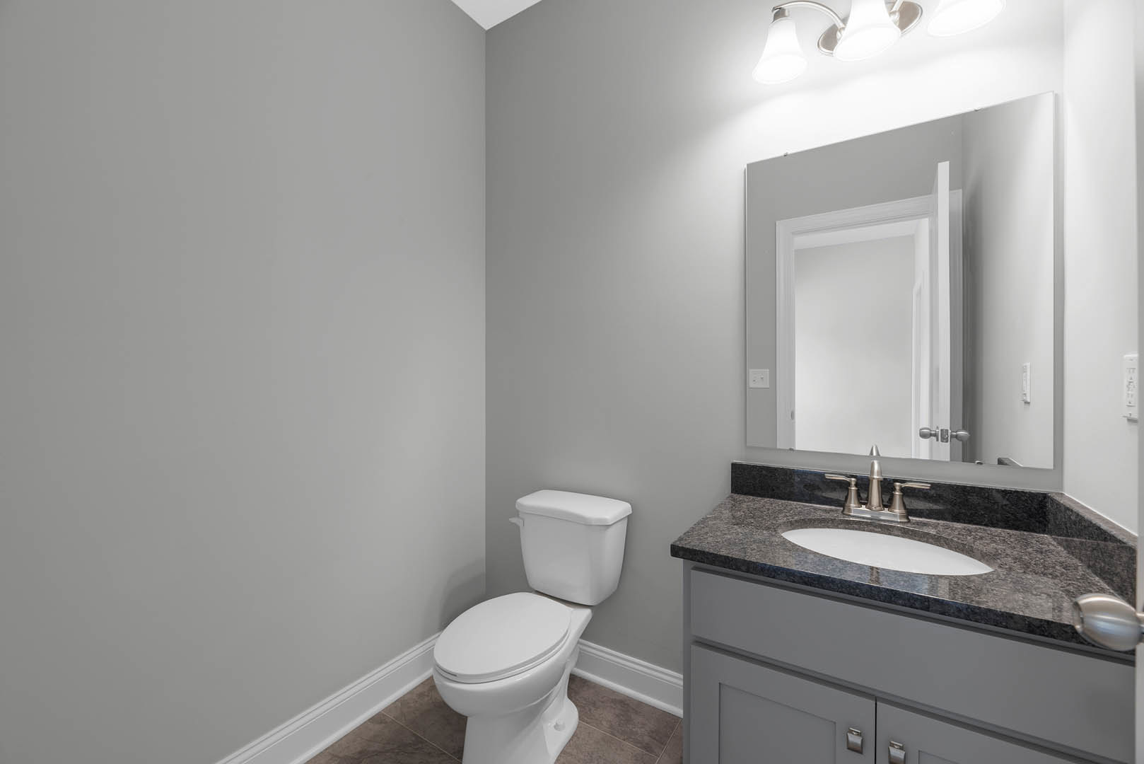 Bathroom with white tile walls, white toilet in the corner, rectangular sink with chrome faucet, wall-mounted mirror, and white door.