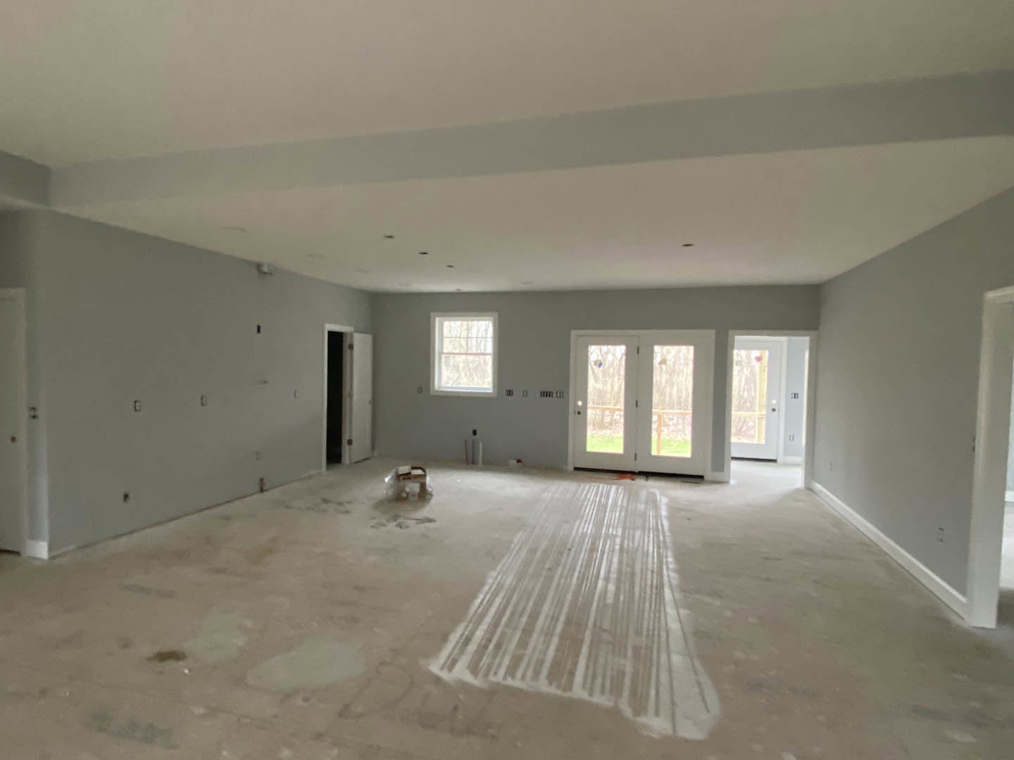 Room with white painted floor, white framed window, double glass pane doors, white door with black hardware, close-up of plastic bag on floor