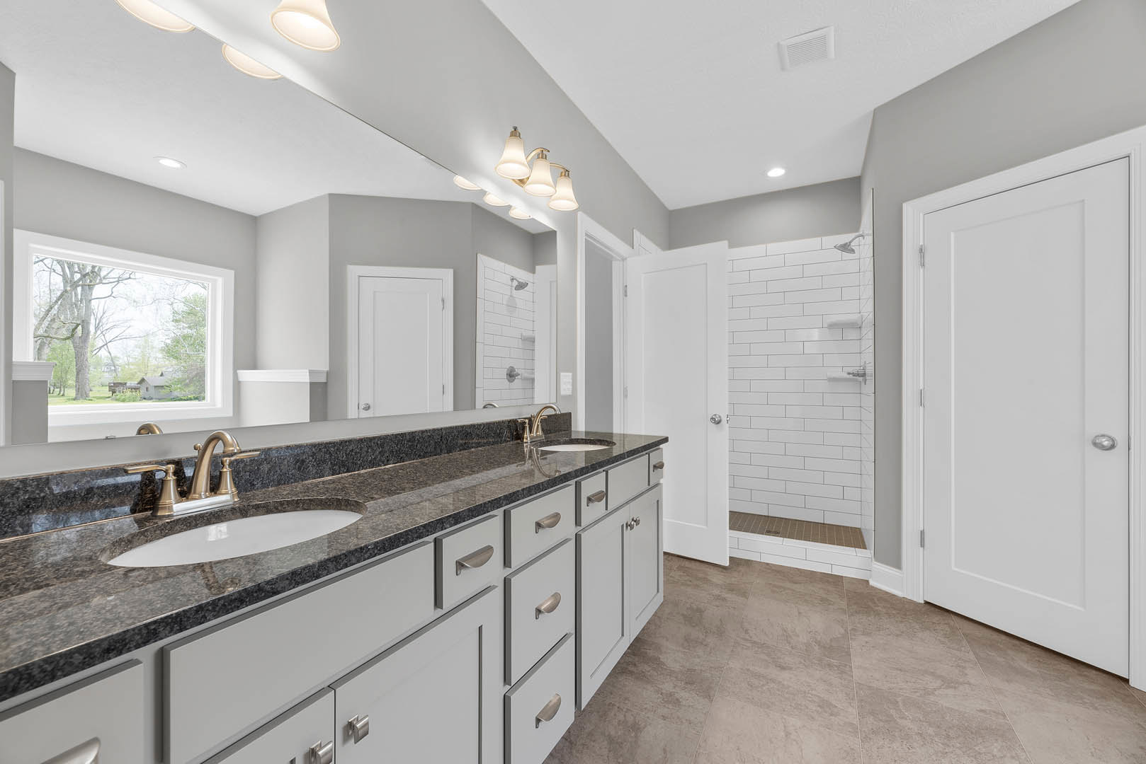 Bathroom with double sink vanity, expansive wall mirror, white cabinetry, silver faucet fixtures, tiled floor, recessed ceiling vent, and modern overhead lighting.