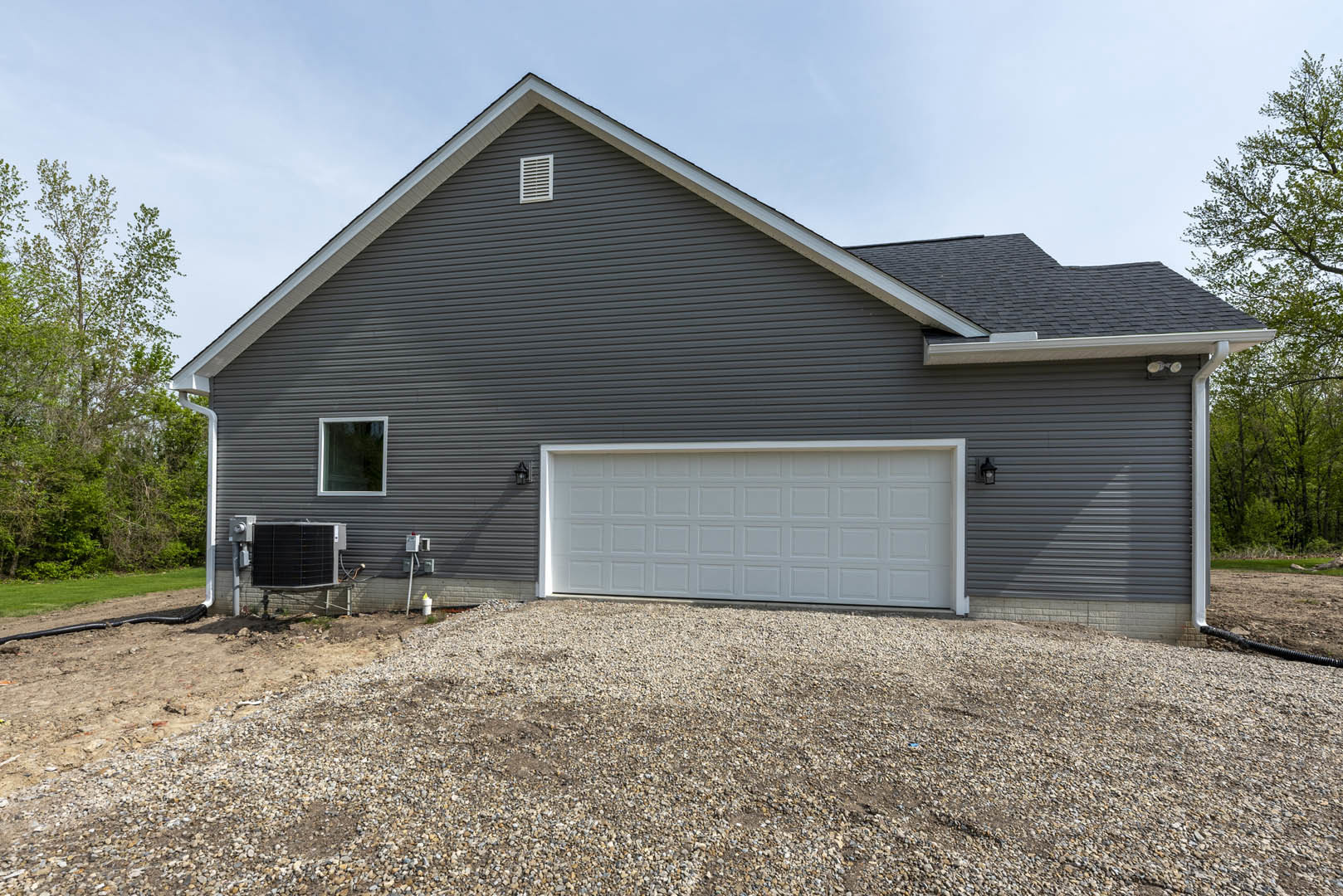 Grey siding house with attached garage, white vent above garage door, gravel driveway, window on front facade, black mailbox mounted on brick wall.