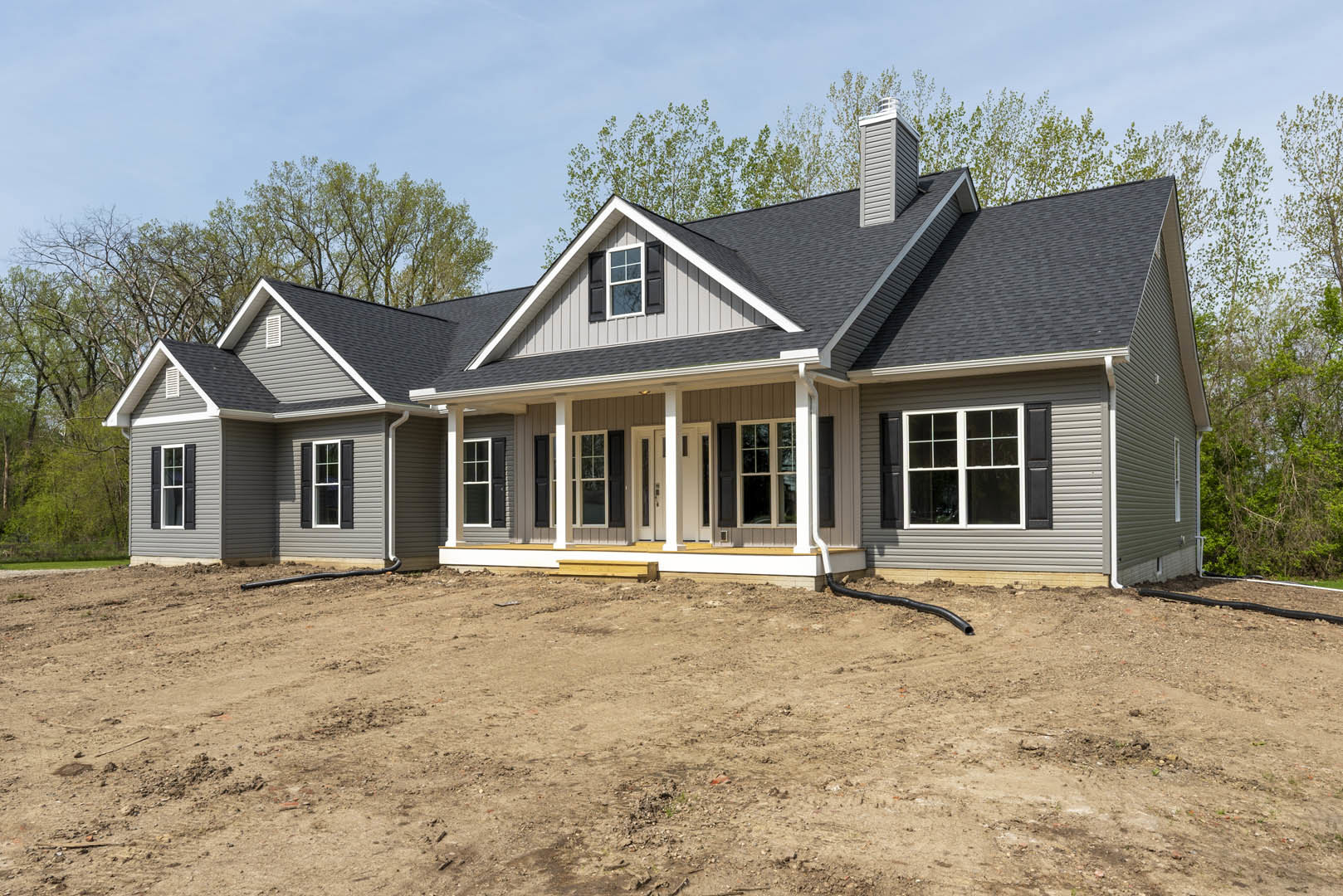 White cottage-style house with horizontal siding, prominent white-framed windows, covered porch, brick chimney, and surrounding dirt yard under a clear sky