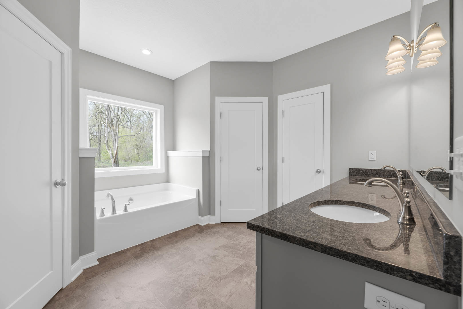 Modern bathroom featuring a freestanding bathtub, white vanity with undermount sink, chrome faucet, tiled walls, large window with tree view, and white door with silver hardware
