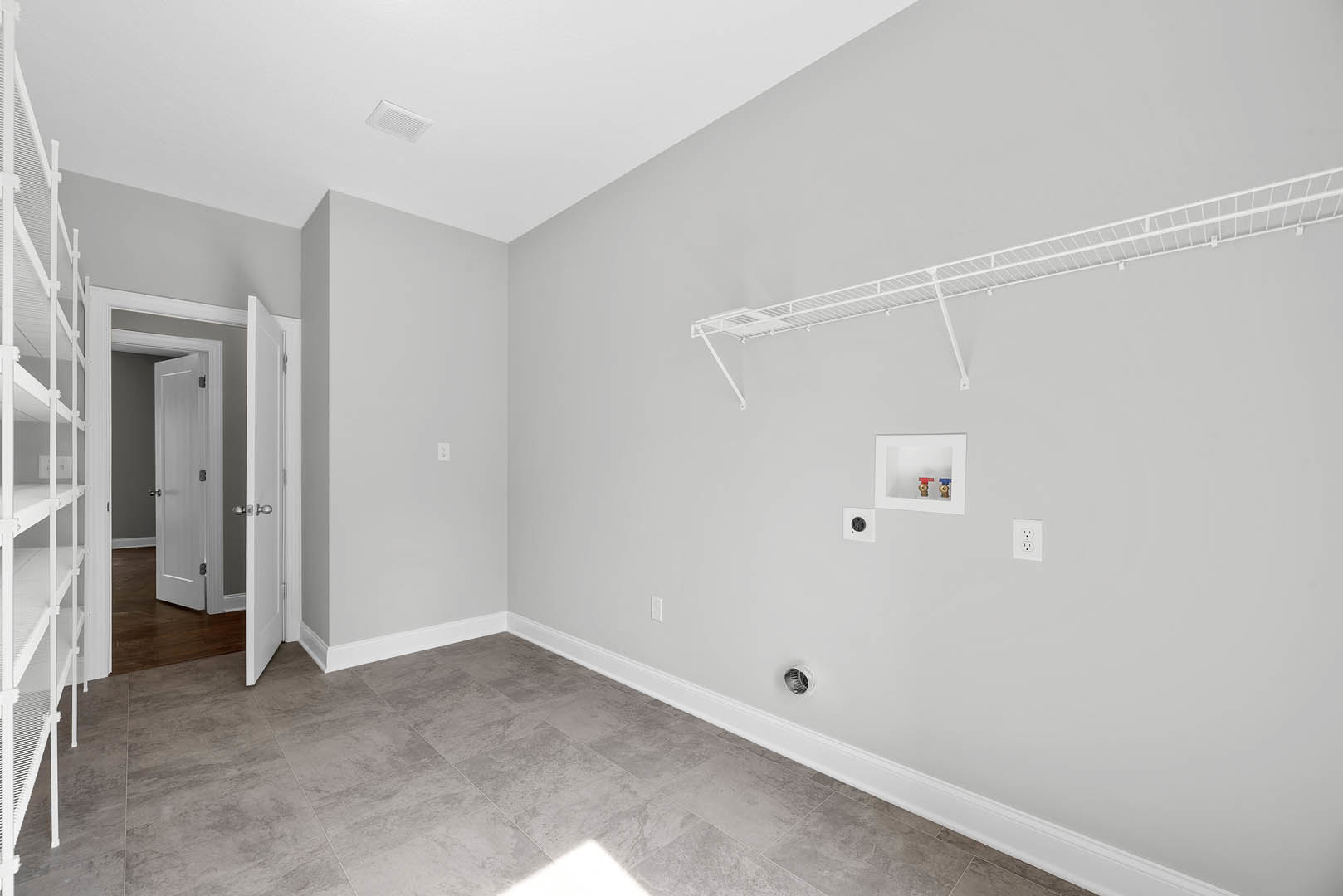Tile floor room with white shelving unit, open white door with silver handle, white metal bar near window, and white utility box with valves against plaster walls.
