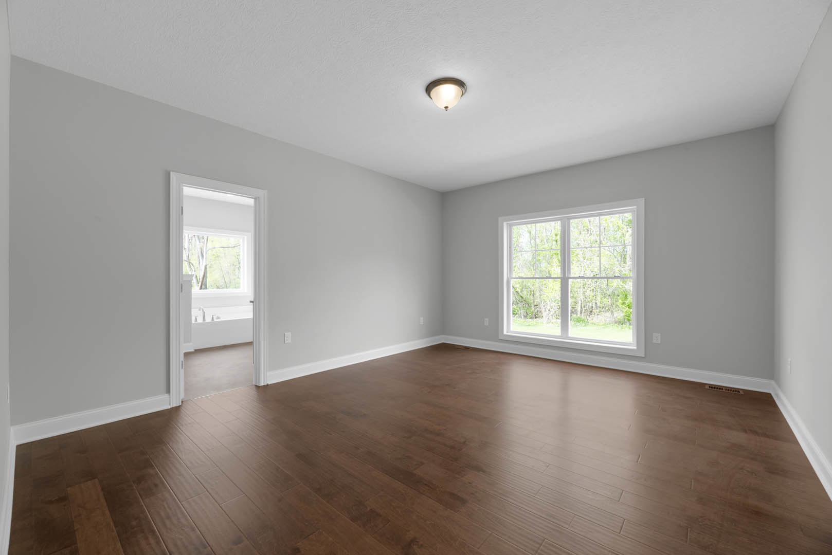 Room with hardwood floor, large window overlooking trees, white walls, ceiling light fixture, and white door with glass panel