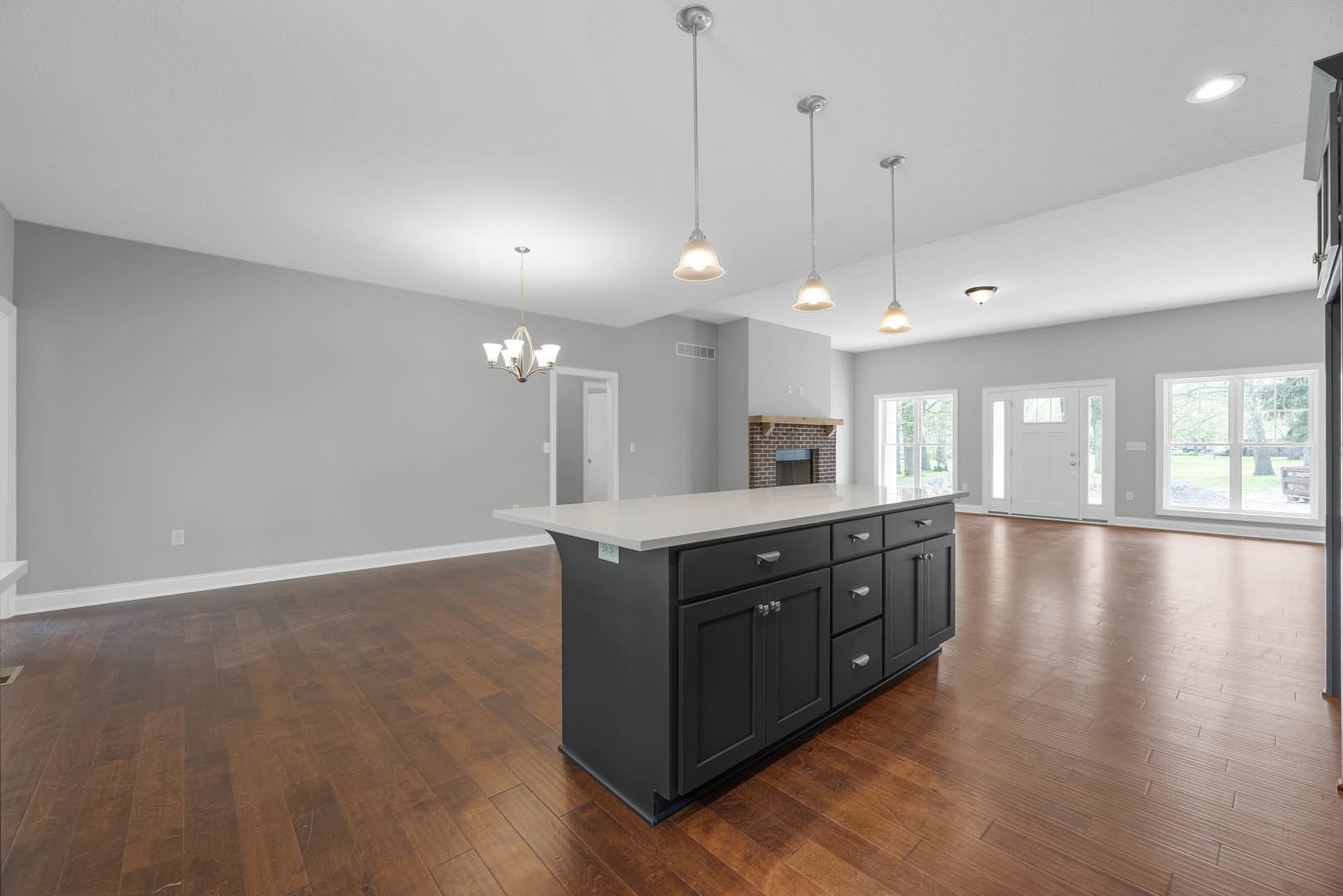 Kitchen island with white countertop and drawers, wood flooring, cabinetry, white door with glass windows, large window overlooking lawn, white and black poles.