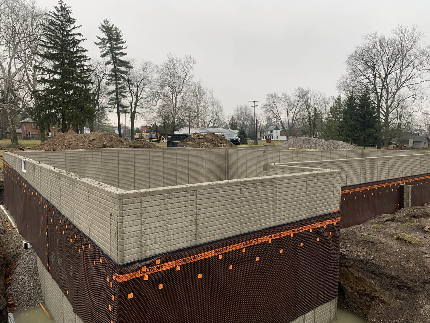 Construction site with piles of dirt, scattered trees, temporary fencing, and clear sky overhead