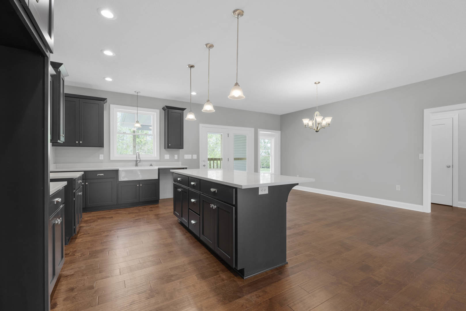 Spacious kitchen featuring a large island with drawers, white sink under ceiling light, wood flooring, black accent wall, and white door with silver handle
