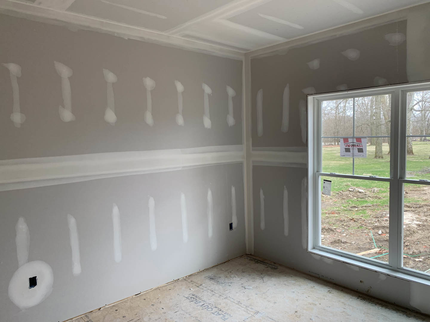 White-painted walls, large window with a red and white sign, white flooring, black square detail, simple molding