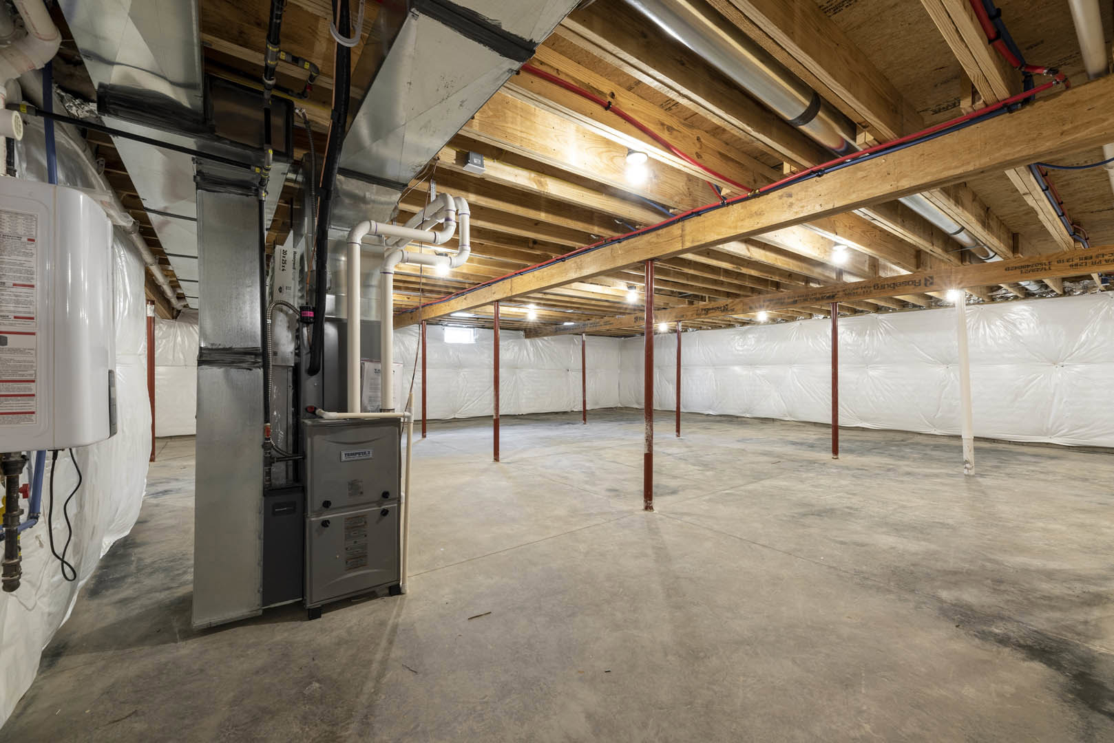 Basement interior with exposed steel beams, white wall, concrete floor, red support poles, ceiling pipes, and recessed lighting.
