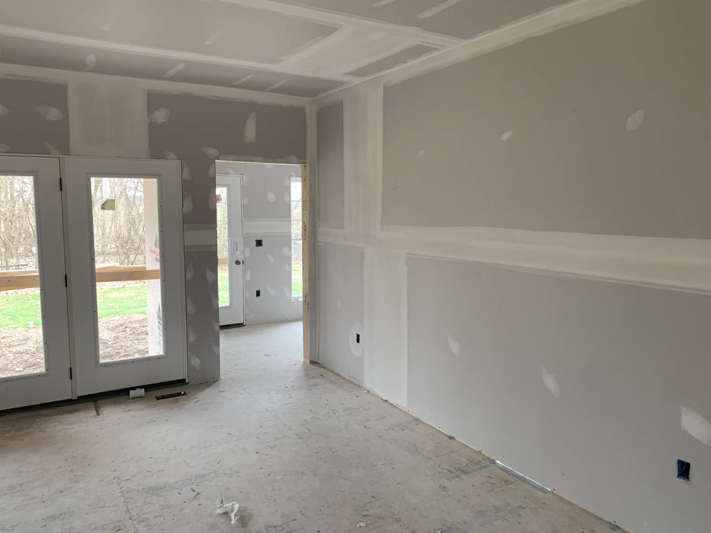 White-walled room with a glass-paneled door, gray flooring, and a blurry dog near a white oval object; person standing in the background.