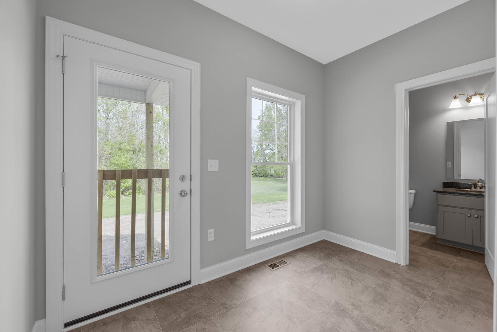 Bright room with white plaster walls, large windows overlooking green lawn, glass-paneled door, wood floor vent, close-up of wood cabinet, and wooden railing visible through