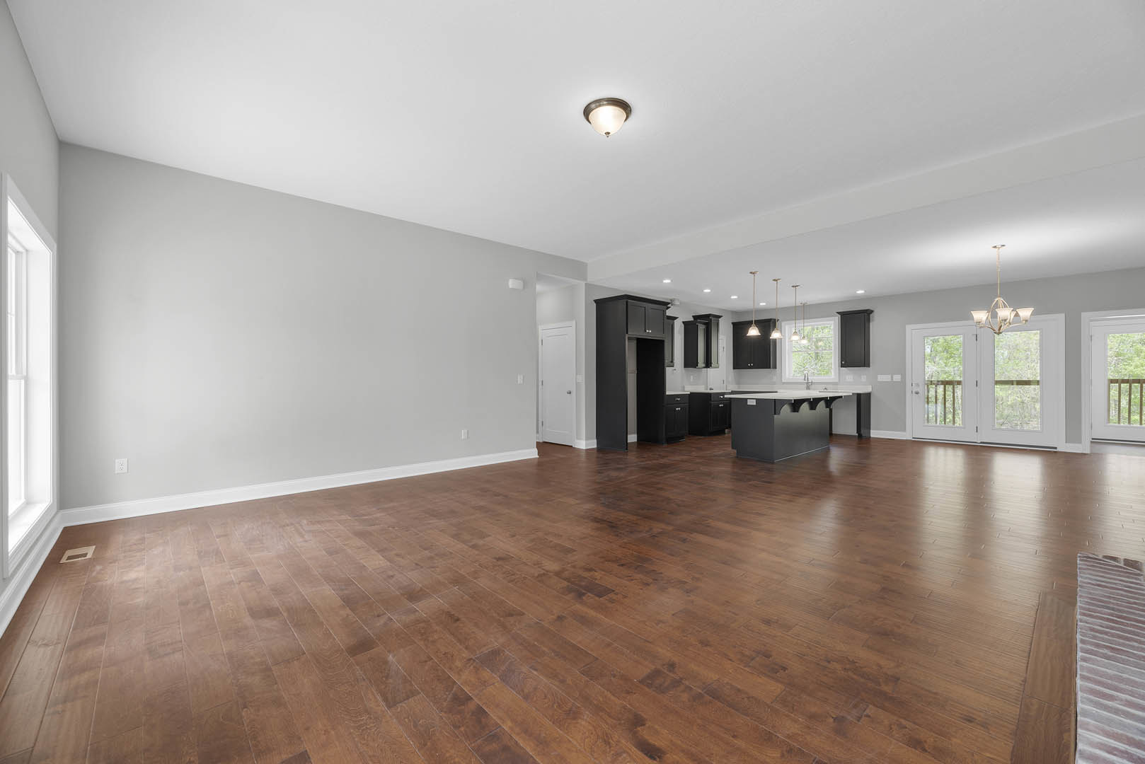 Open-concept kitchen and dining area with hardwood floors, white-framed window, ceiling light fixture, and chandelier.