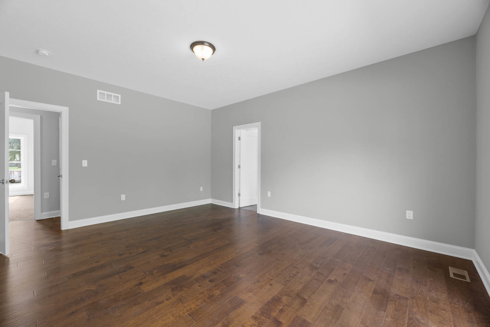 Hardwood floor room with white framed door, ceiling light fixture, white railing, and wall vent