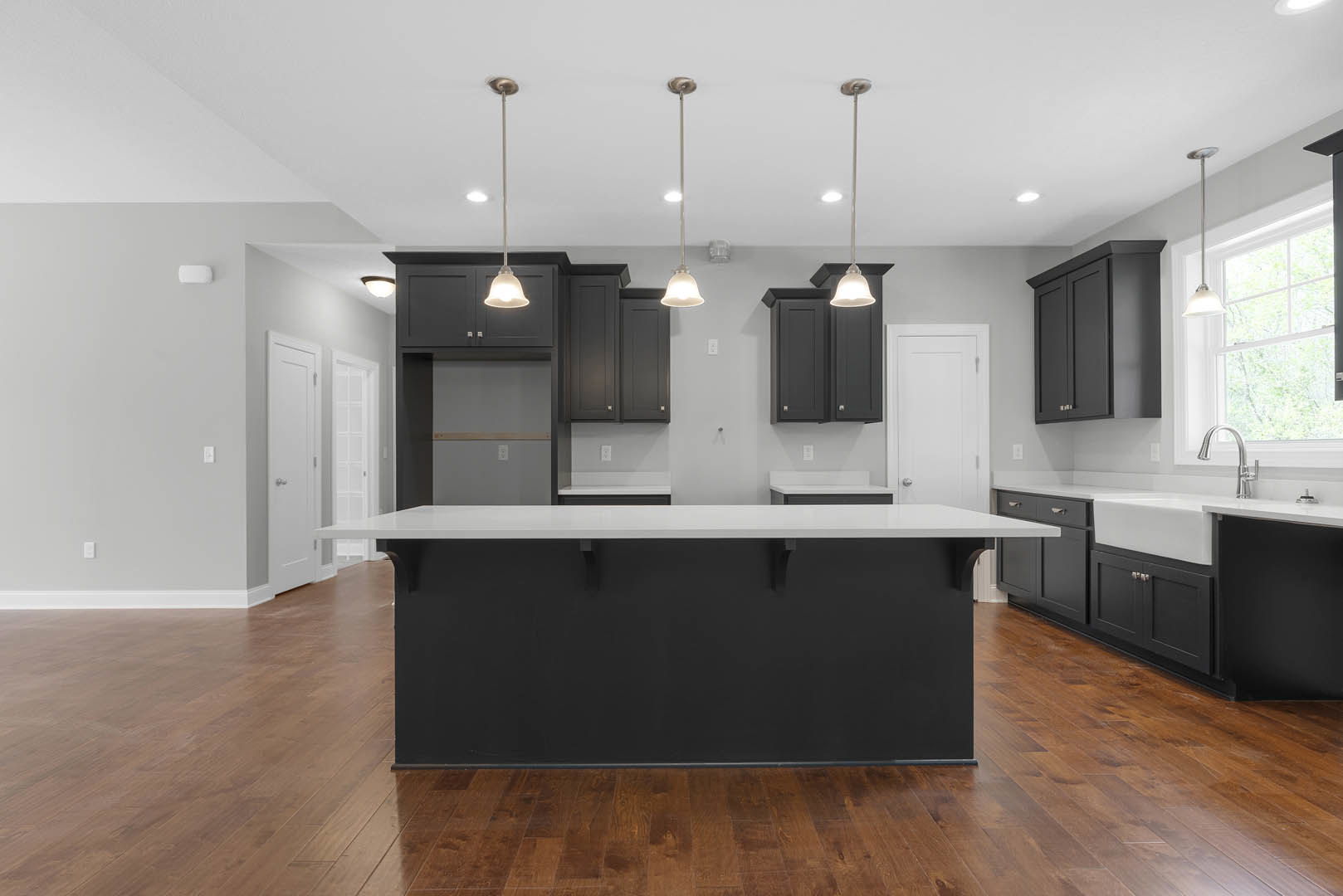 Modern kitchen featuring a central island with black and white countertops, black cabinetry, white walls, wood flooring, ceiling-mounted light fixture, and a pole light.