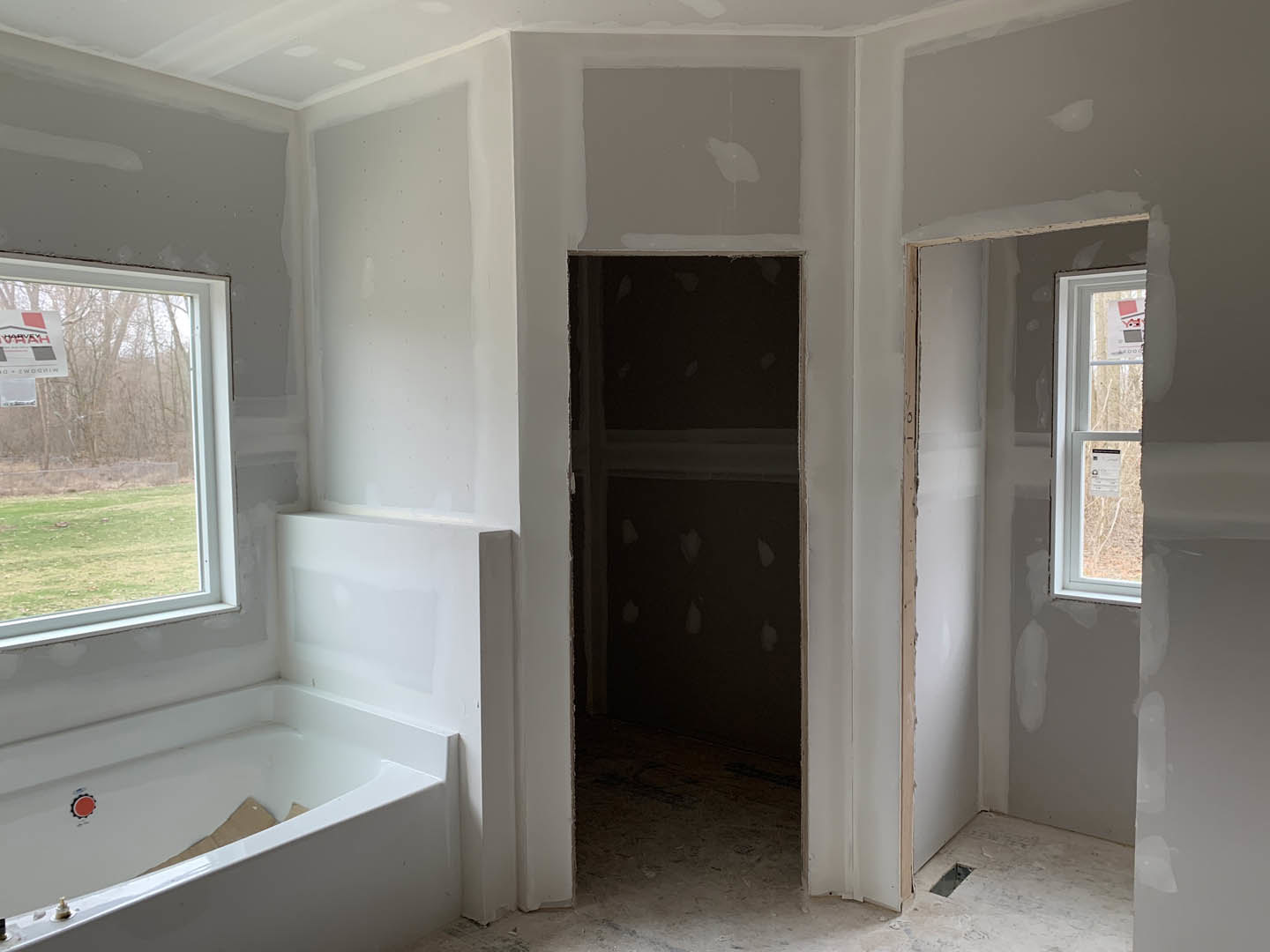 Bathroom with freestanding tub, open door, window with paper sign, white shelf with black handle, cardboard piece inside bathtub, plaster walls