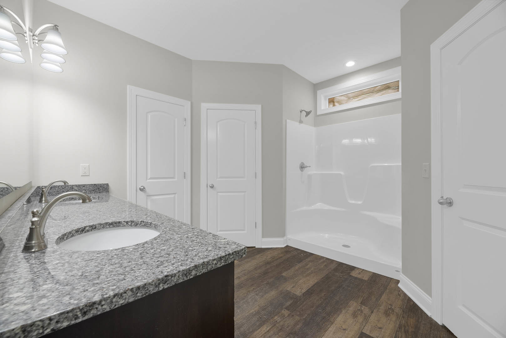Bathroom featuring a marble countertop with undermount sink and chrome faucet, glass-enclosed shower with silver handle, white door with silver knob, and modern light fixture above