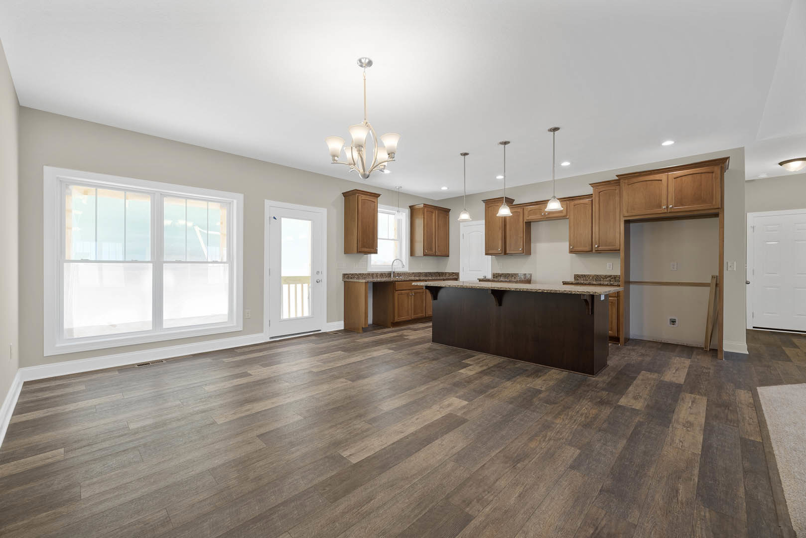 Spacious kitchen featuring a large marble-topped island, wood flooring, white cabinetry, modern chandelier, and a white door with a window