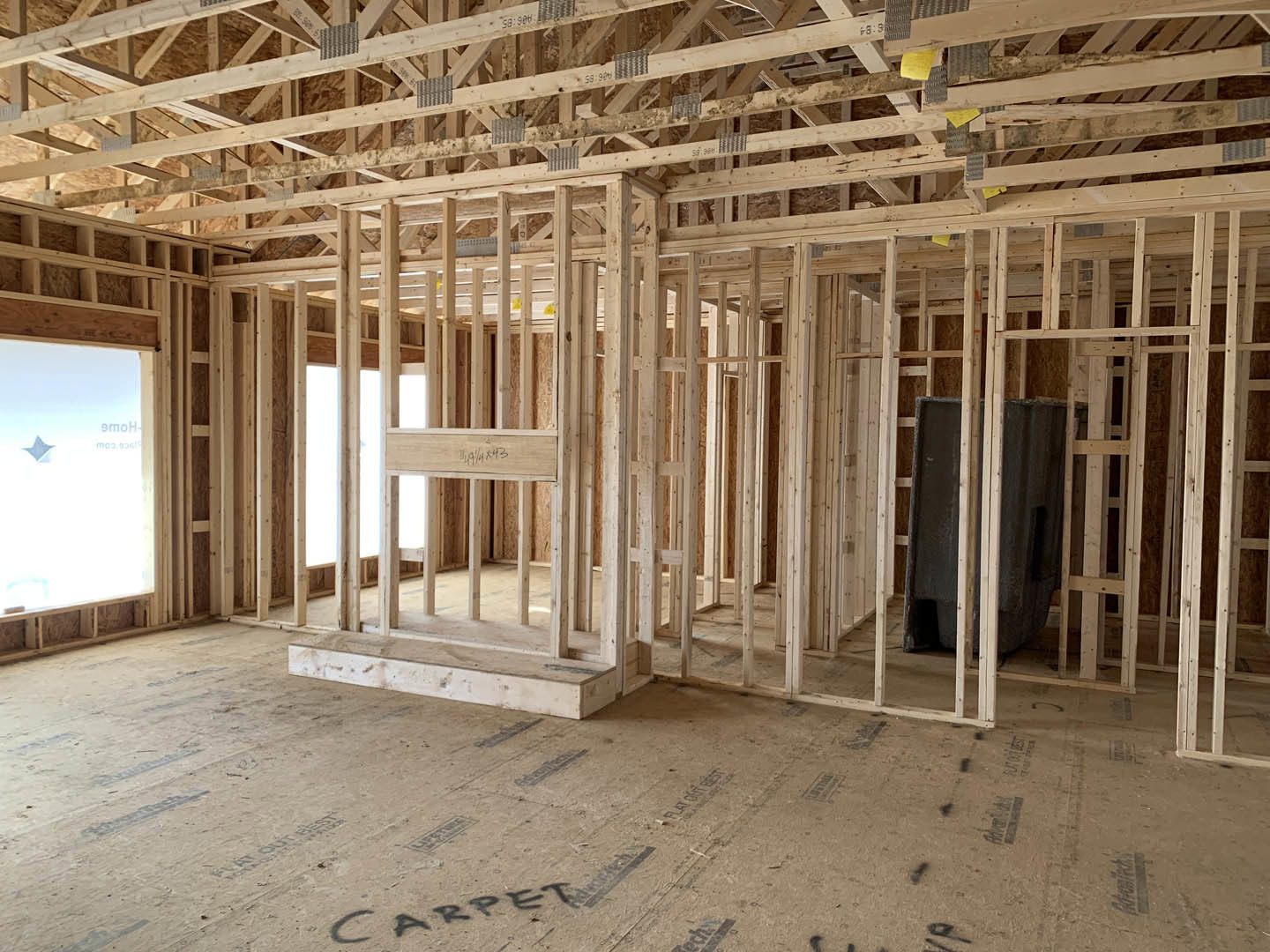Exposed wood framing with beams, unfinished walls, and ceiling, construction materials scattered on subfloor, window opening visible