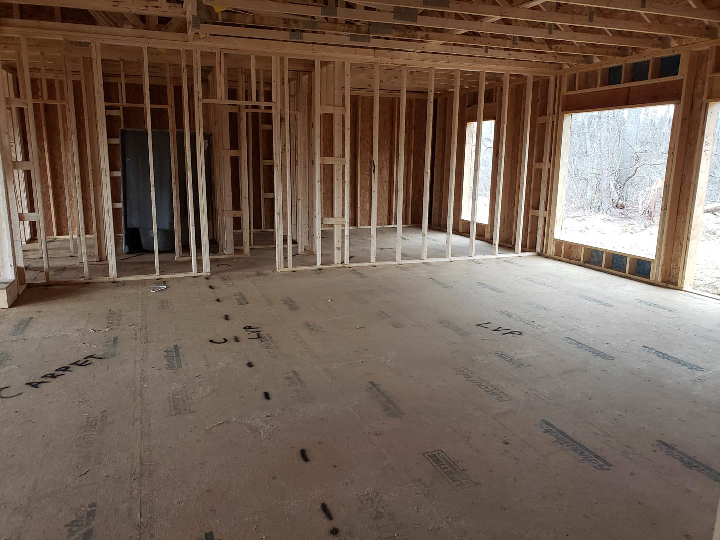 Wood-framed room with exposed beams, black accent wall, ceiling insulation, large window overlooking forest, and stone detail