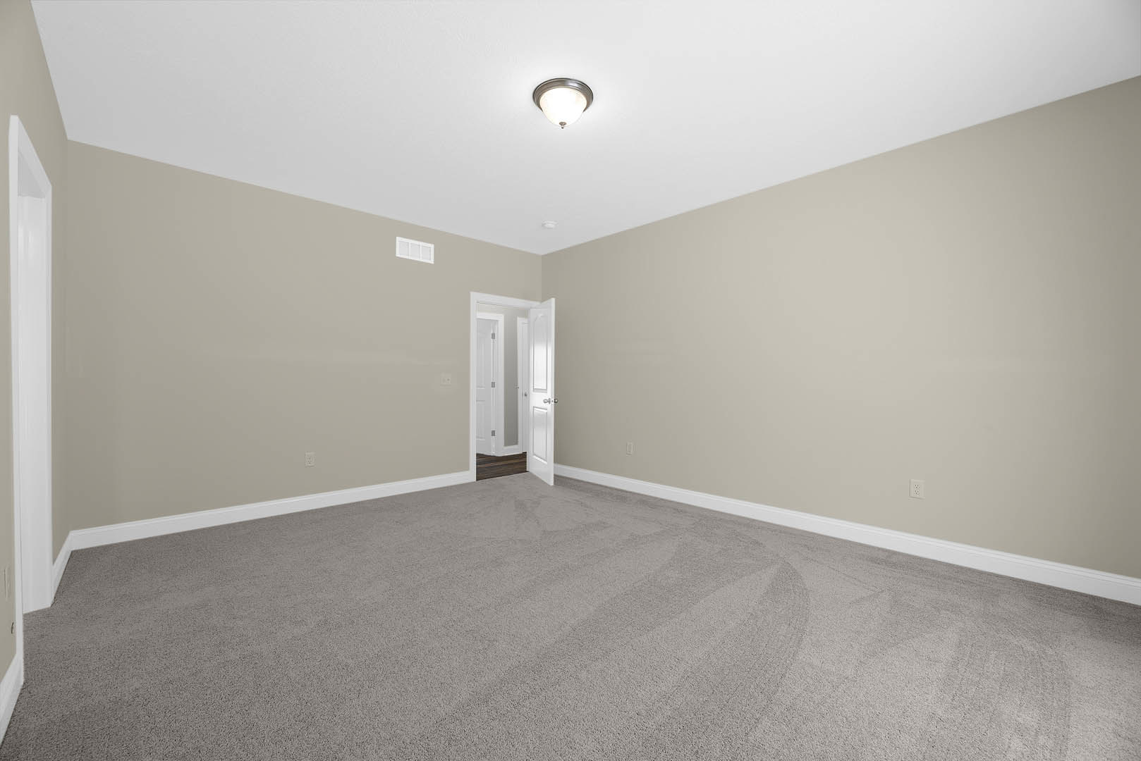 Carpeted room with white walls, open white door with silver knobs, ceiling light fixture, white baseboards, and black-bordered rectangular object on wall