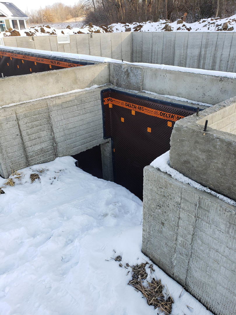 Concrete wall with central metal gate, snow covering ground and roof, winter exterior of residential home