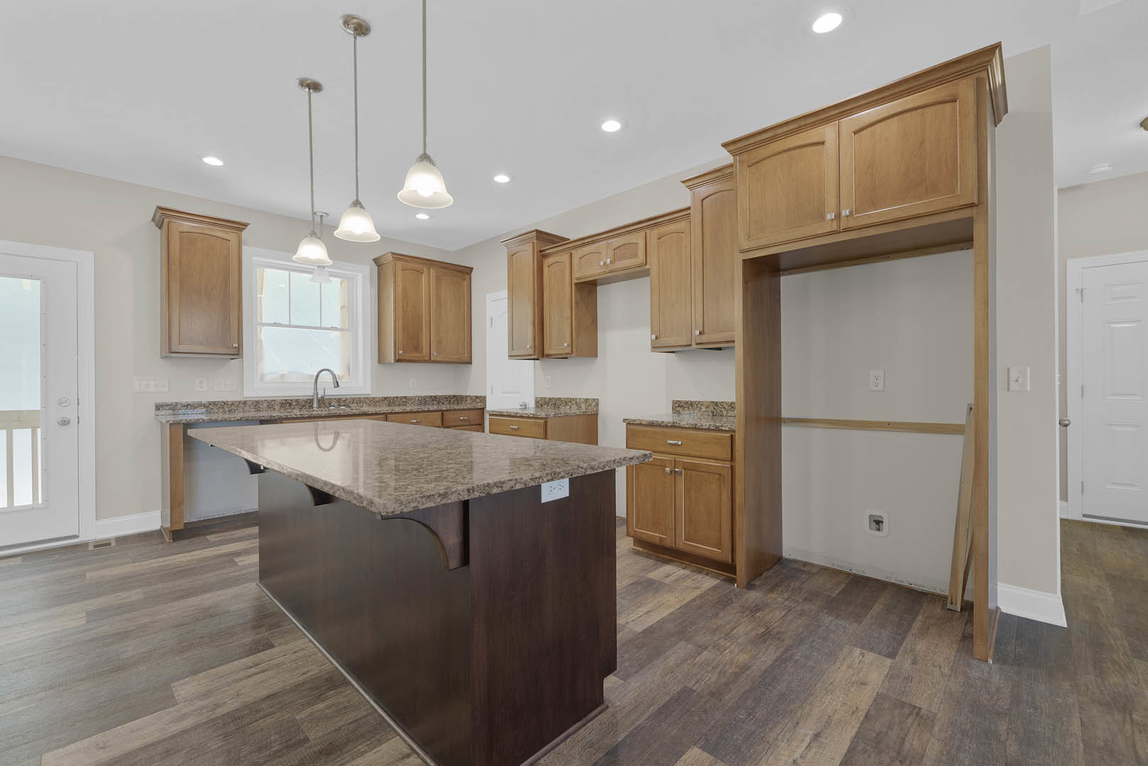 Spacious kitchen featuring a large central island with granite countertops, white cabinetry, tile flooring, stainless steel faucet, and a white sink.