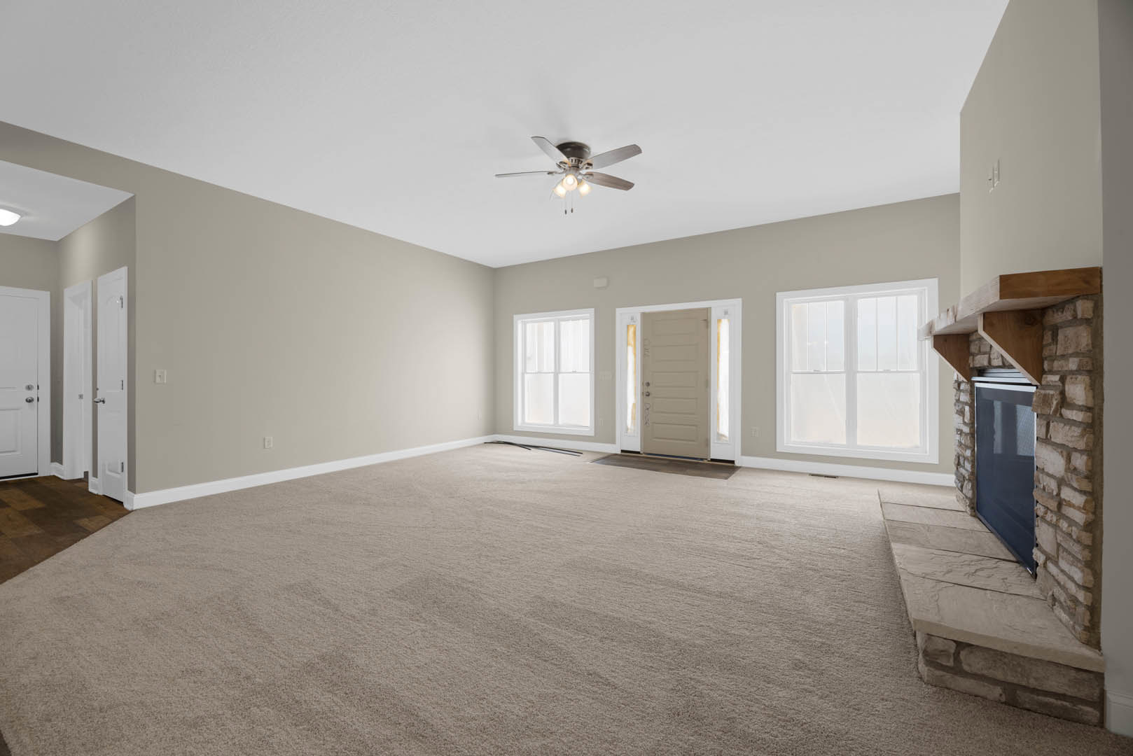 Carpeted room with white walls, ceiling fan with lights, white door featuring glass panes, and a window letting in natural light