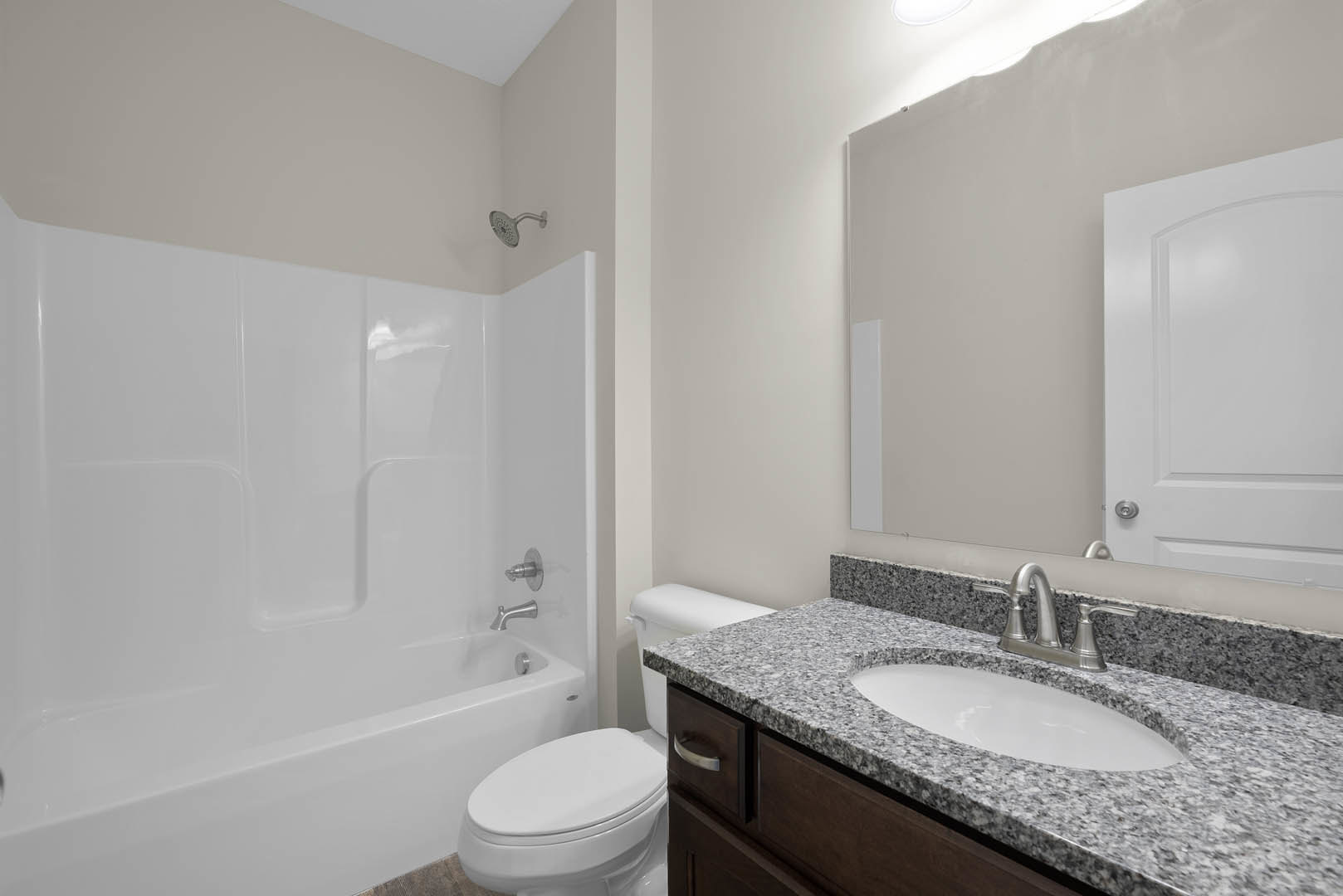 Bathroom with white ceramic sink and silver faucet, closed white toilet, glass-enclosed shower with chrome showerhead, light tile walls and floor.