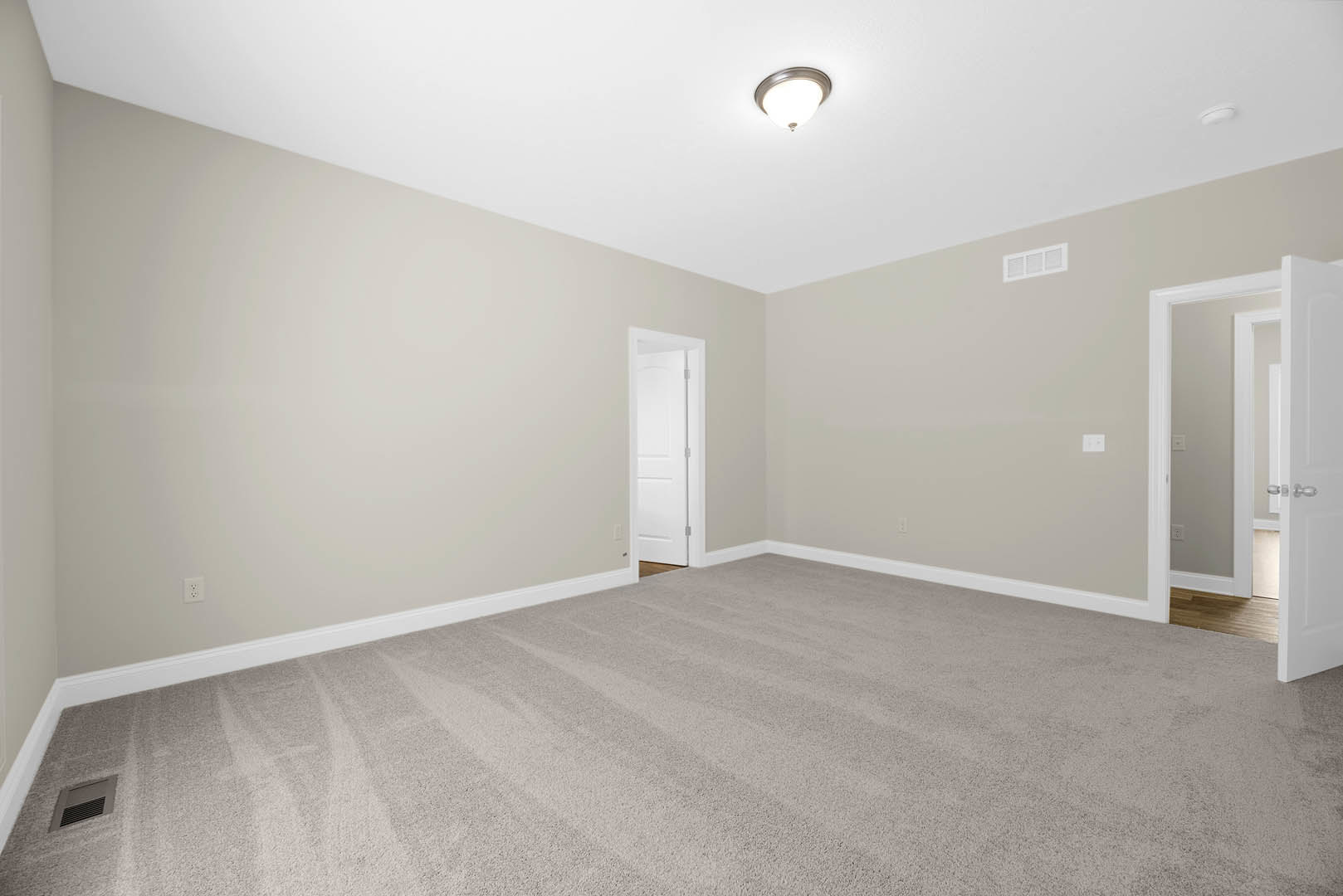 Carpeted room with white walls, open white door with silver handle, ceiling-mounted light fixture, and white wall vent