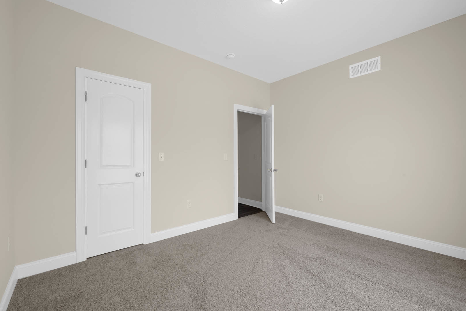 White paneled door with silver handle open to carpeted room, white walls, ceiling vent, and crown molding