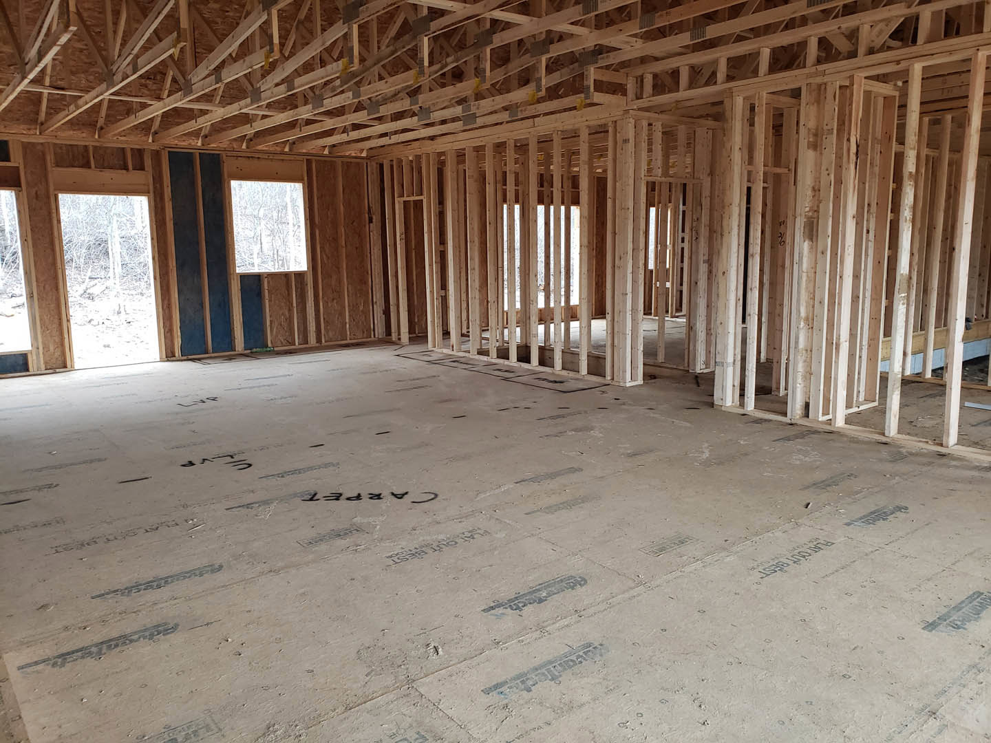 Living room with exposed wood ceiling beams, large window overlooking snowy ground, light-colored walls, and hardwood flooring