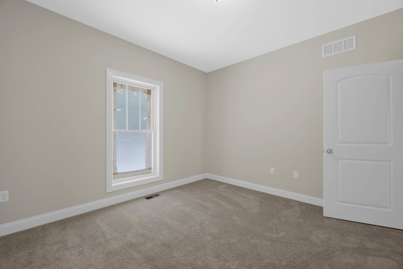 Neutral-toned carpeted room with white walls, large window with white trim, white door featuring a silver handle, wall vent, and simple baseboard molding
