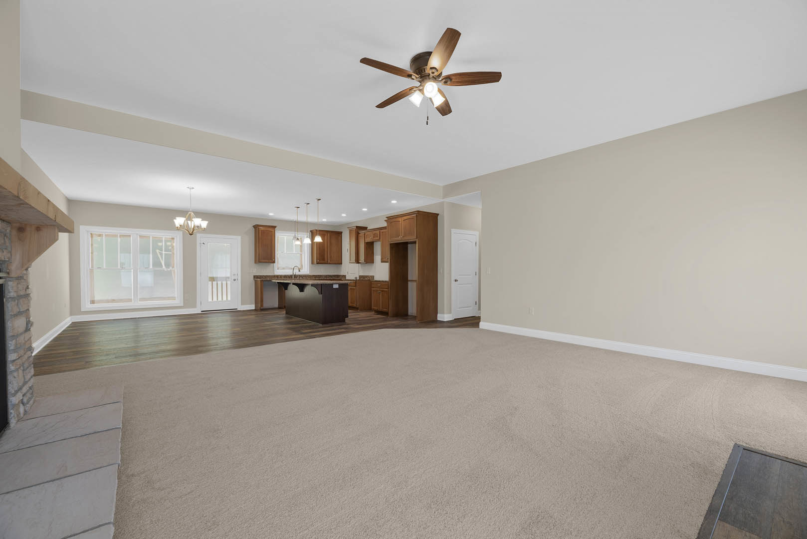 Open-concept kitchen and dining area with light-colored walls, ceiling fan with lights, glass-paned window, white doors including one with glass panels, and carpeted flooring