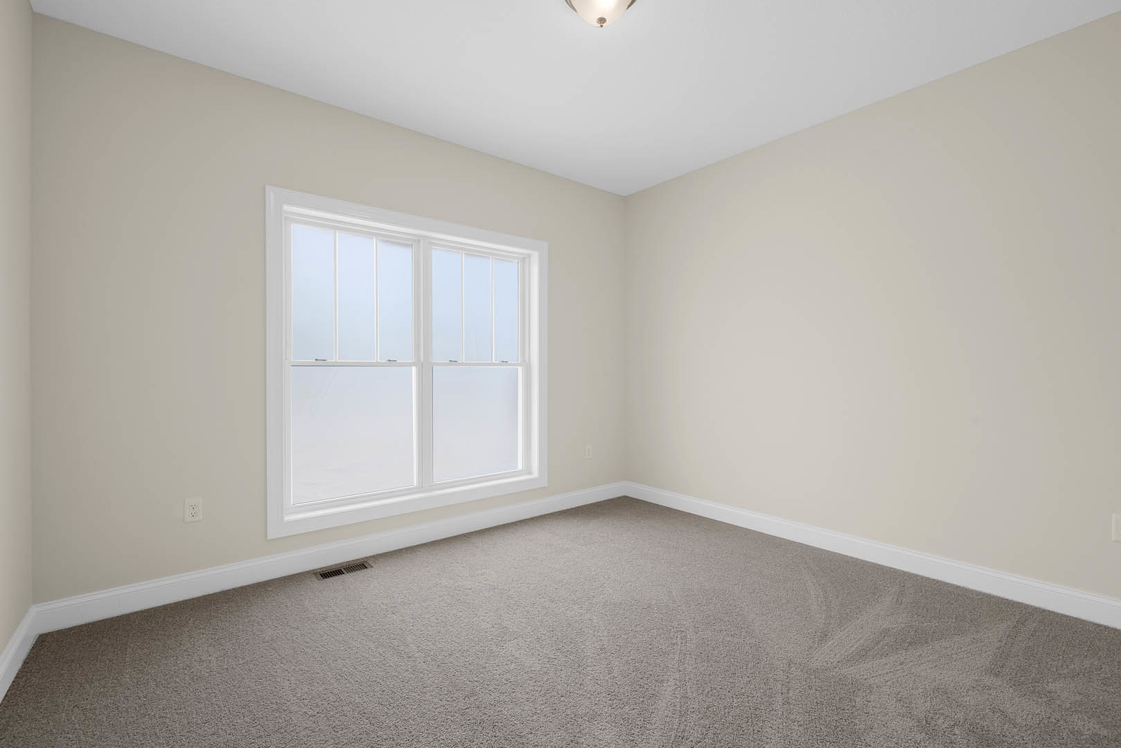 Neutral-toned carpeted room with white walls, large frosted glass window, white ceiling featuring recessed light, and a decorative box with black and red ribbon placed near the