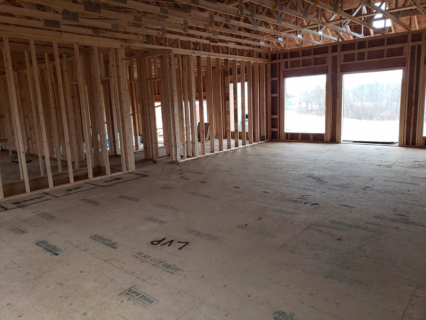 Unfinished room with exposed wood ceiling beams, large window overlooking snowy forest, bare walls and floor