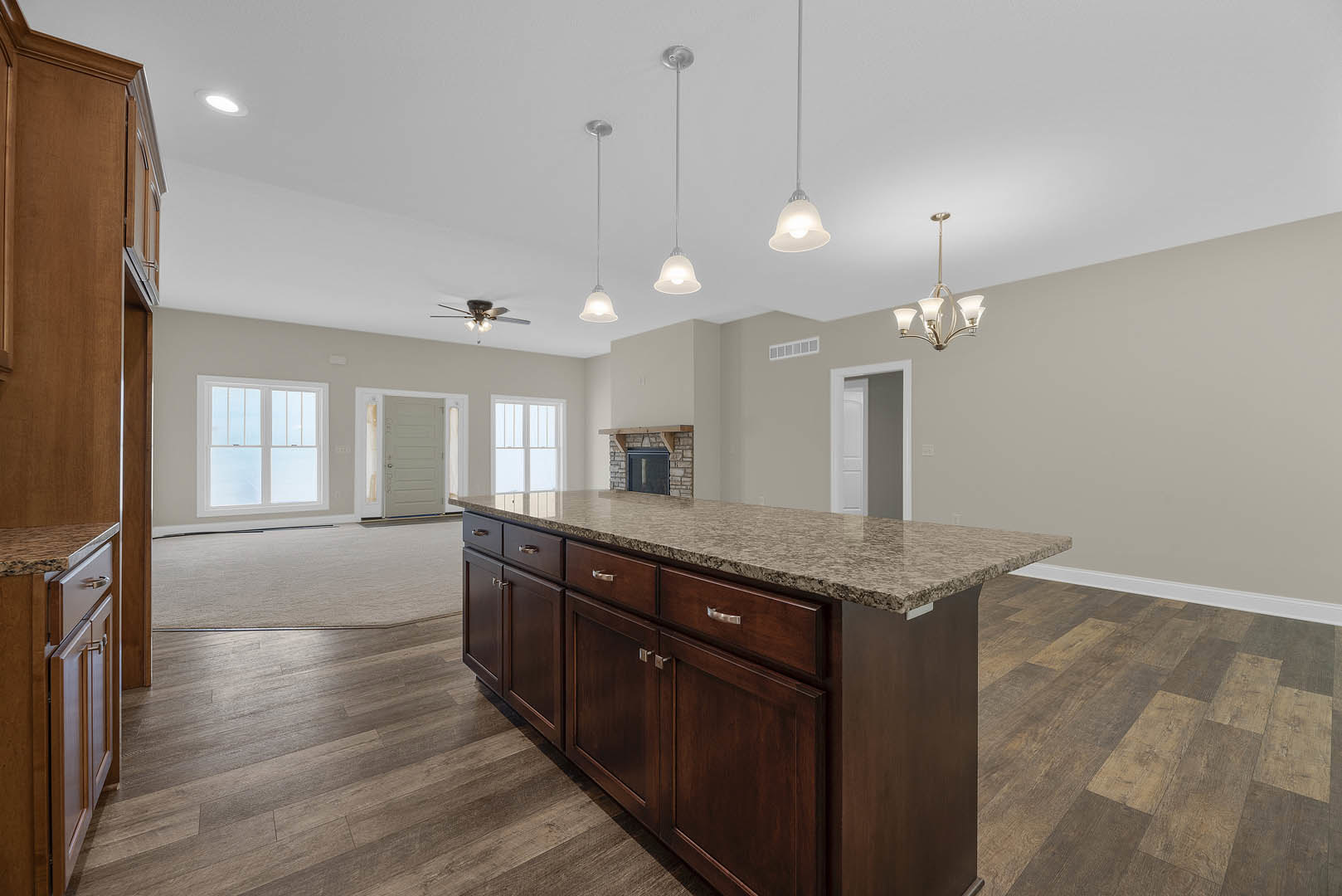 Granite kitchen island with built-in sink, white cabinetry, hardwood flooring, pendant chandelier, and nearby window and door with glass panels