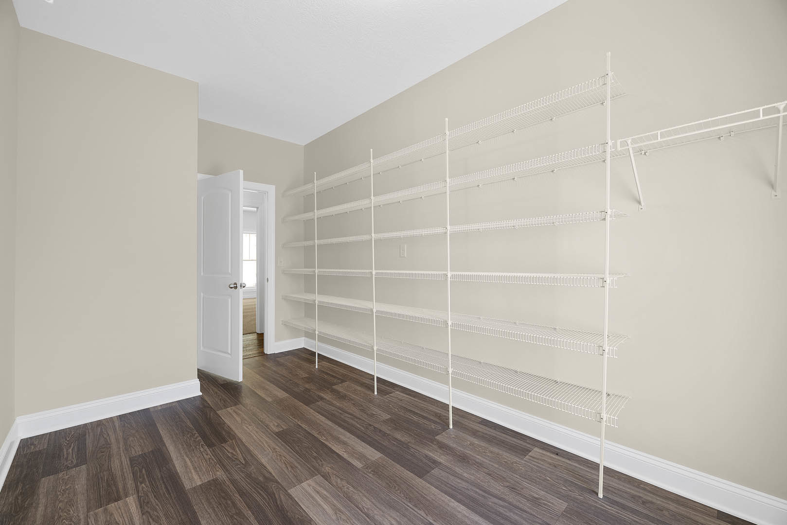 White built-in shelves against a white wall, wood flooring, white curtain, and white door with silver knob in a bright room.