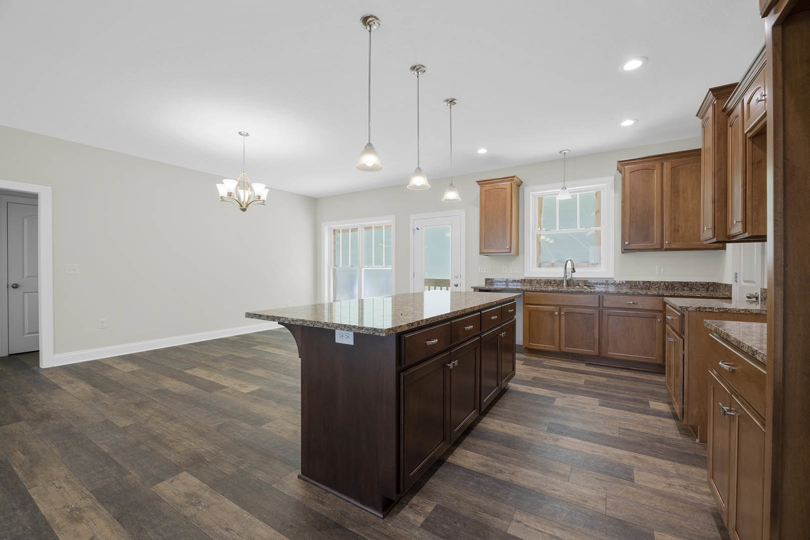 Spacious kitchen featuring a large central island with granite countertops, white cabinetry, stainless steel appliances, pendant lighting, and a white door with glass window.