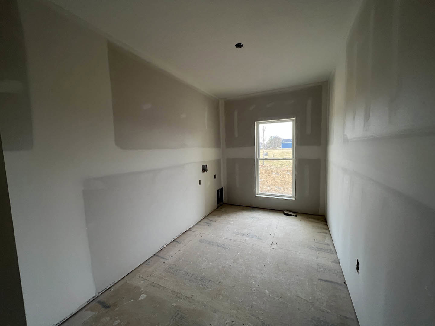 Sunlit room with smooth concrete floor, white plaster walls, and large window overlooking a blue barn in the distance