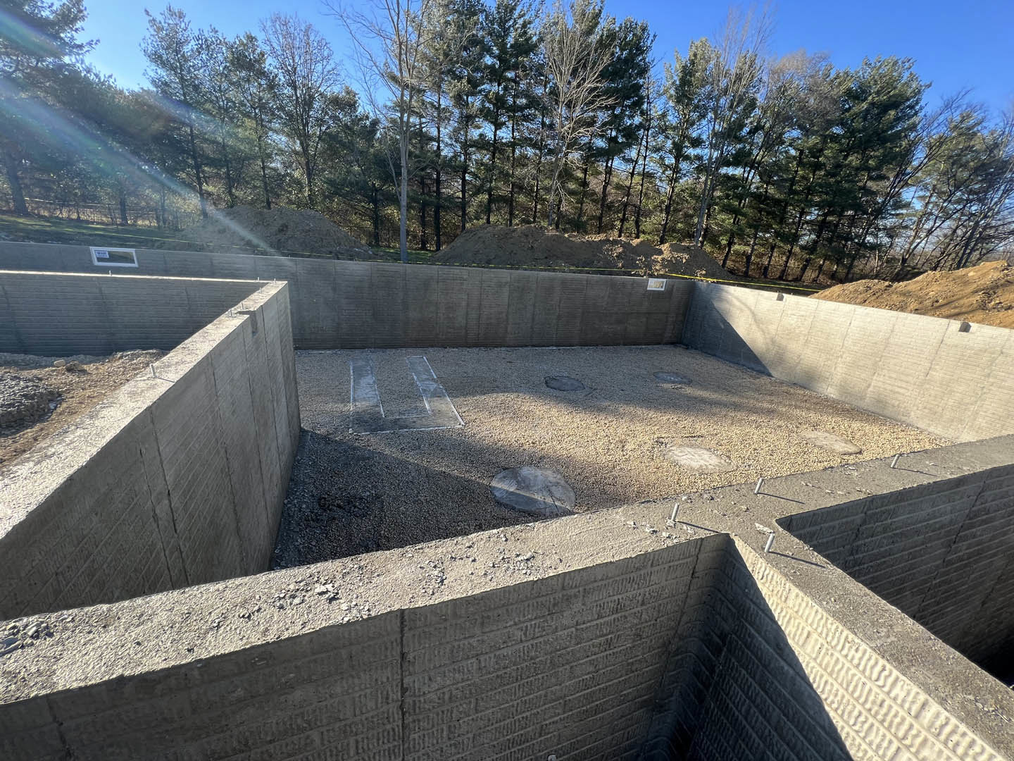Concrete foundation surrounded by gravel and rocks, with trees and sky visible in the background