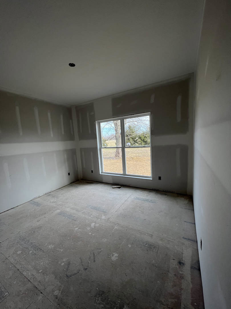 Concrete-floored room with plaster walls, large window framing leafy tree view, black ceiling fixture