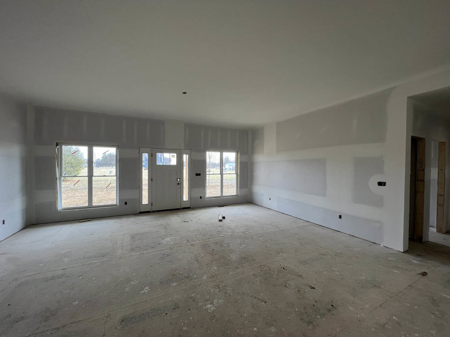 White-walled room featuring a white door with glass panes, large window with white frame, light-colored flooring, and plaster ceiling.