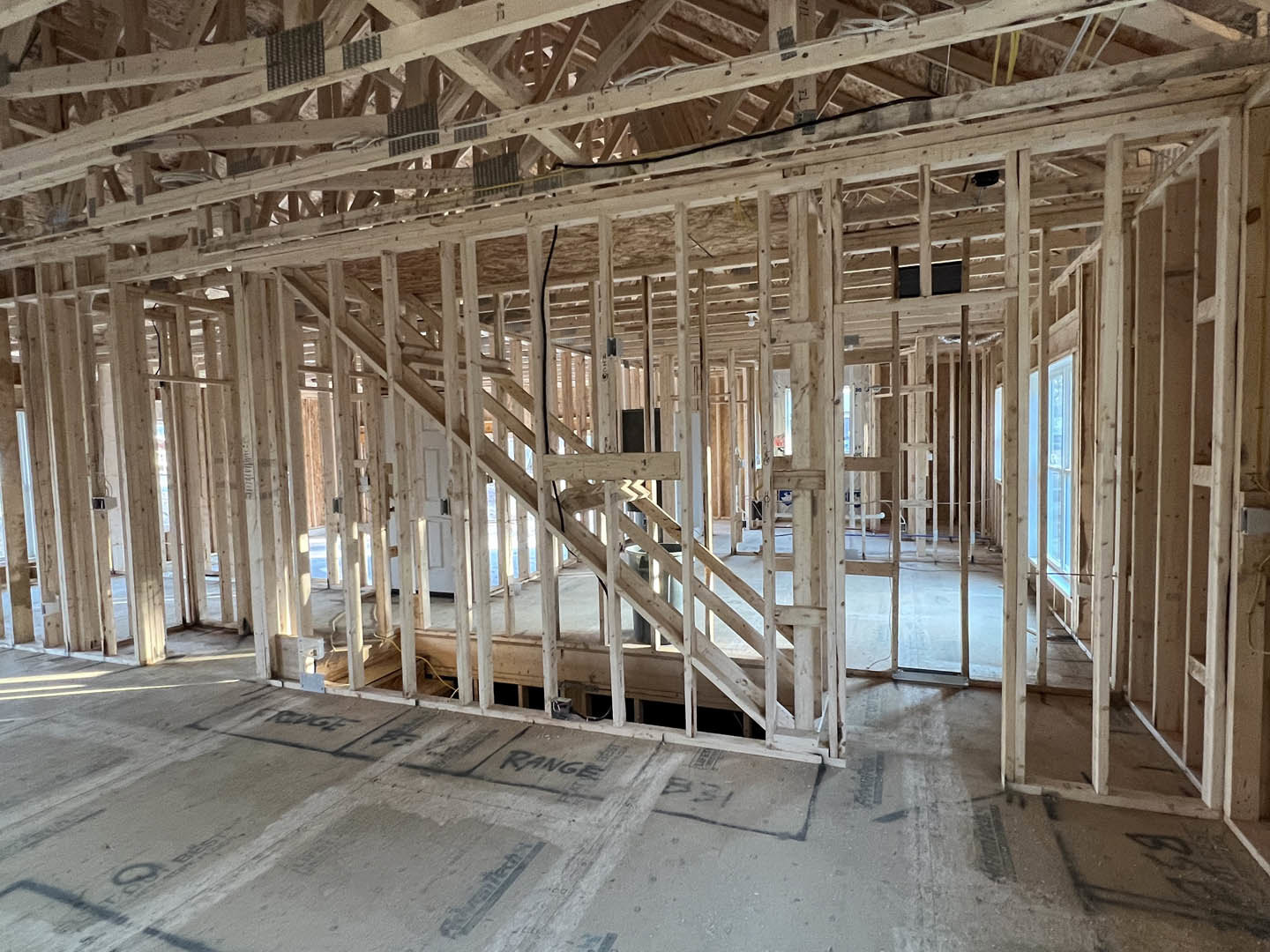 Exposed wood framing and beams inside a house under construction, sunlight casting circular shadow on unfinished floor