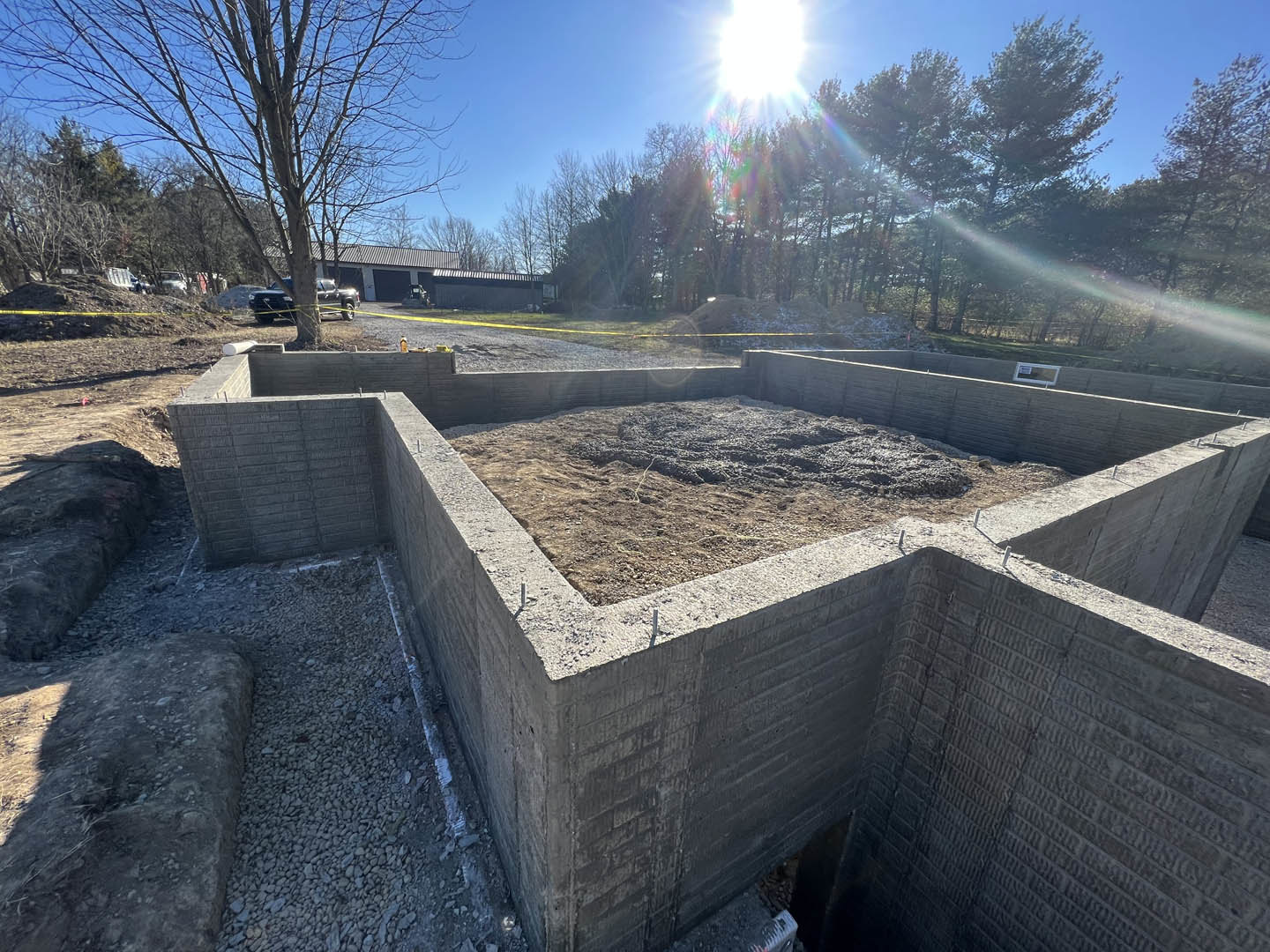 Concrete foundation with exposed dirt center, surrounded by bare ground and trees under bright sunlight