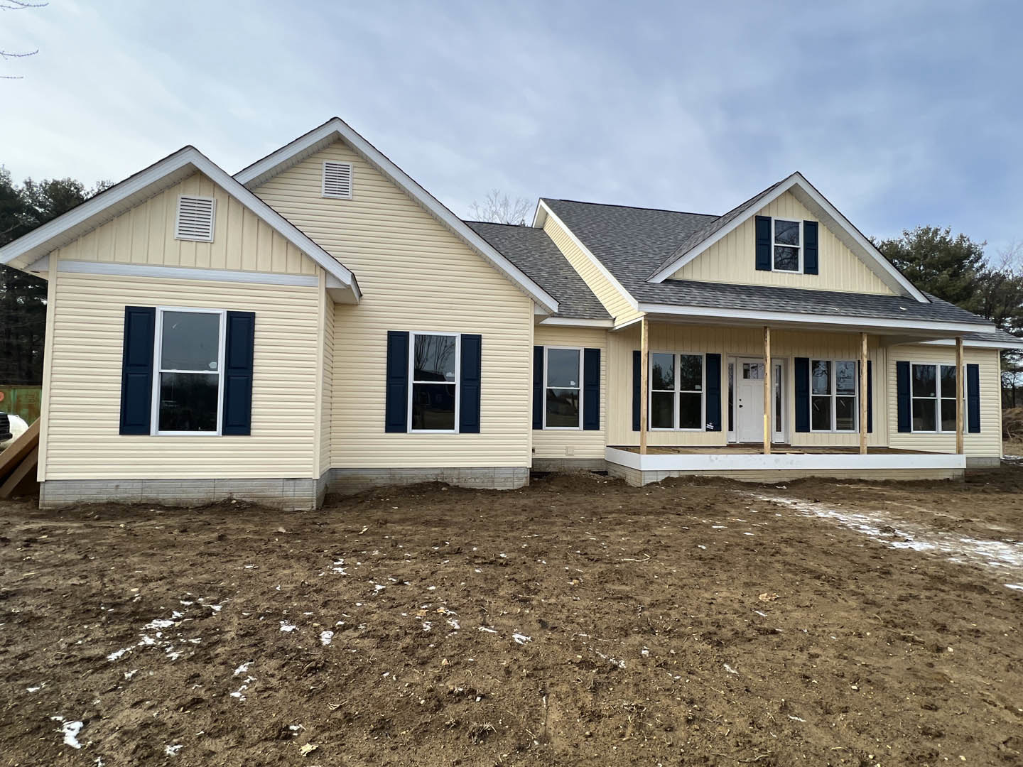 White and brown dirt yard in front of a house with light siding, white-framed windows, wall vent, and broken glass in one window under a cloudy sky