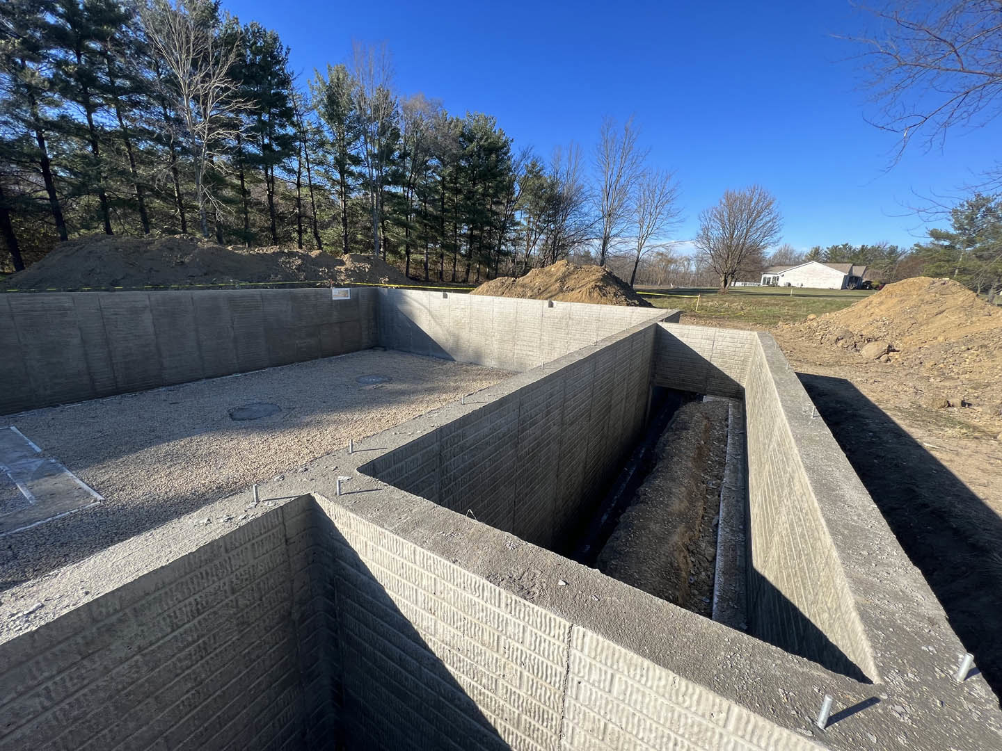 Concrete foundation with exposed hole in the ground, leafless tree nearby, blue sky and The Pentagon visible in the background